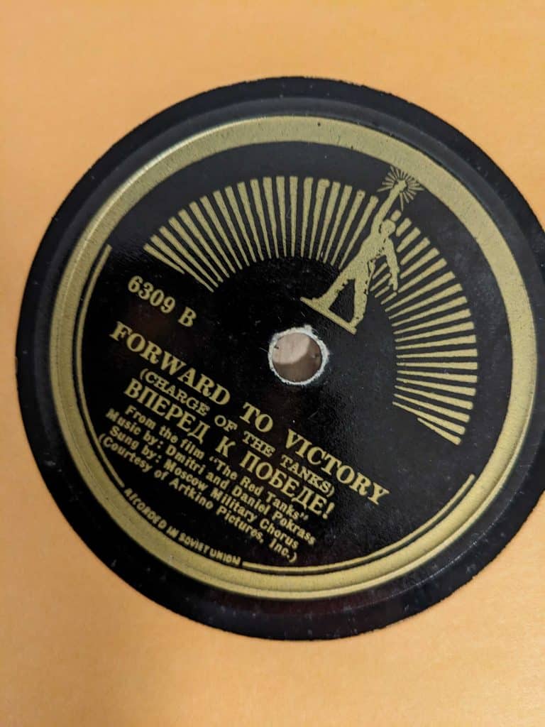 Forward To Victory label. Lettering in gold against a black background. Outline of soviet worker at top above spindle.